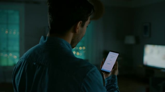 年轻英俊的男人在他的智能手机上向智能家居应用程序发出语音命令，房间里的灯正在打开。他对技术印象深刻。