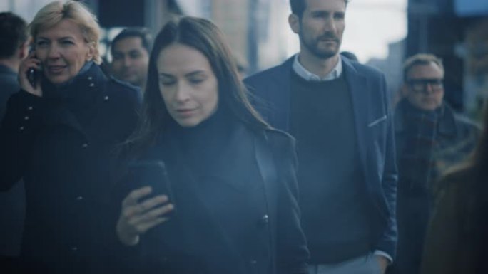 穿着黑色外套的美丽女商人正在市中心的街道上使用智能手机。她走在拥挤的步行街上，看起来很成功。她正在用
