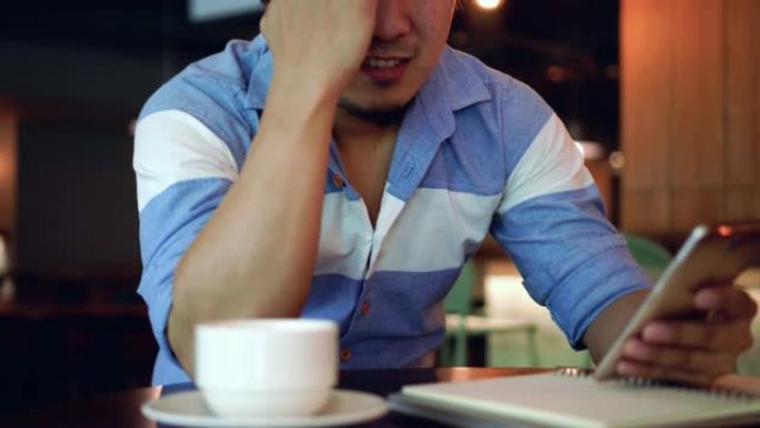 4k镜头亚洲商人穿着休闲服工作和患有抑郁症的场景与智能手机在共同工作空间，商业健康和压力概念
