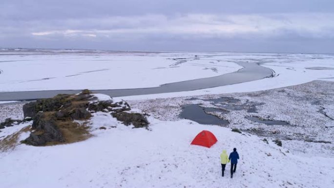 夫妇走向悬崖上的帐篷，俯瞰着冰岛偏远的冰雪覆盖的风景