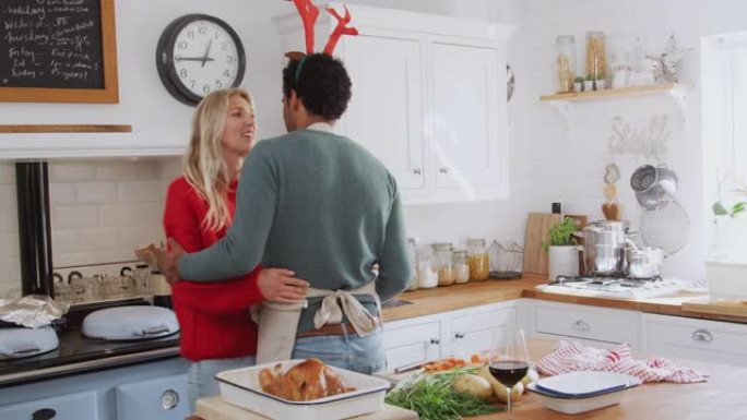 亲爱的夫妇穿着化装礼服鹿角在厨房跳舞，同时准备圣诞晚餐