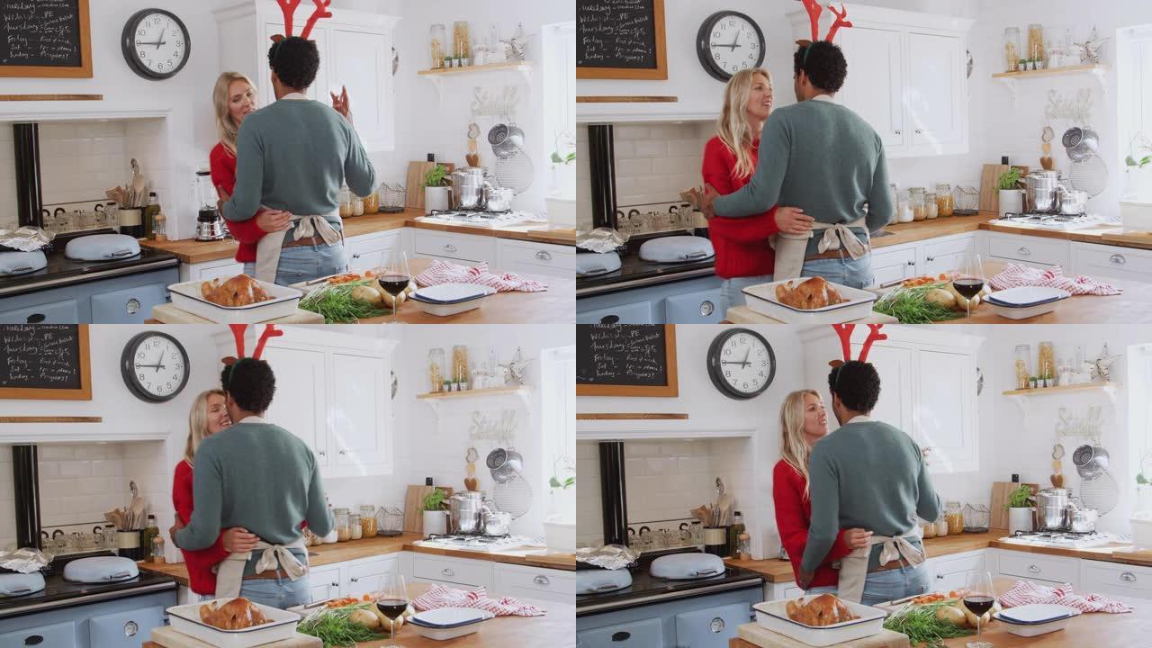 亲爱的夫妇穿着化装礼服鹿角在厨房跳舞，同时准备圣诞晚餐