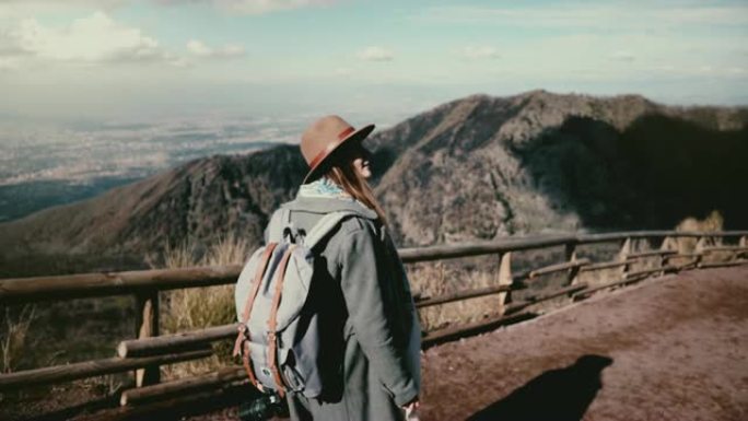 年轻开朗的旅游女孩带着相机从维苏威火山徒步旅行，转身微笑。