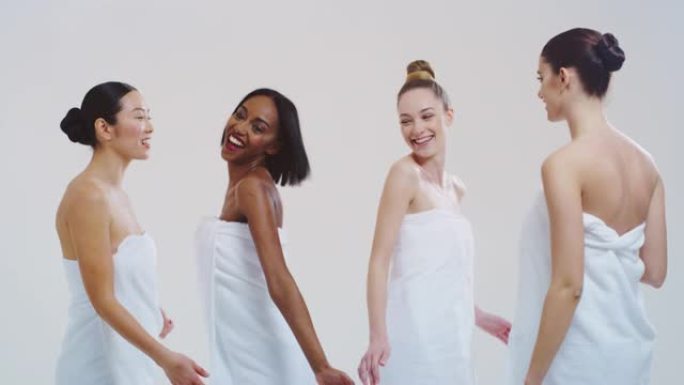 不同种族的美丽年轻微笑女性的慢动作，完美结实苗条的身体，穿着白色浴巾跳舞，享受孤立在白色背景上的乐趣