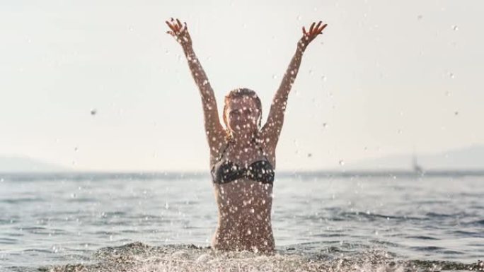 海滩假期中顽皮的女人以慢动作将海水溅向相机