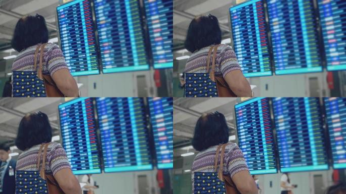 亚洲高级女性在抵达离境板上检查和查看航班