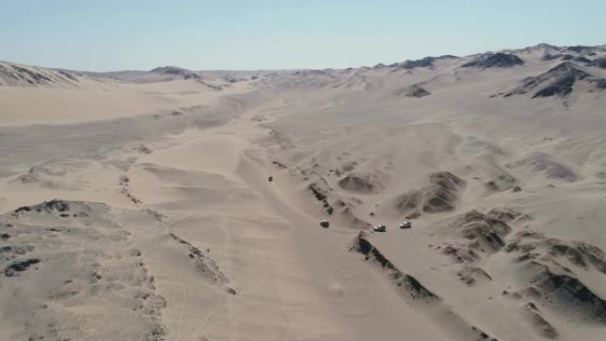 纳米比亚纳米布沙漠骨架海岸上4x4车辆车队在沙丘和山脉之间行驶的4k空中平移视图