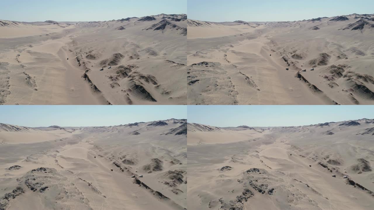 纳米比亚纳米布沙漠骨架海岸上4x4车辆车队在沙丘和山脉之间行驶的4k空中平移视图