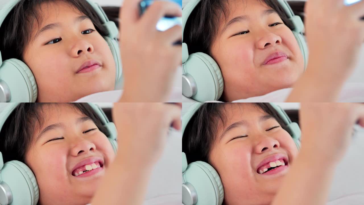 小女孩在耳机中使用智能手机，同时躺在n bed.edu阳离子，儿童，技术，科学和人的概念