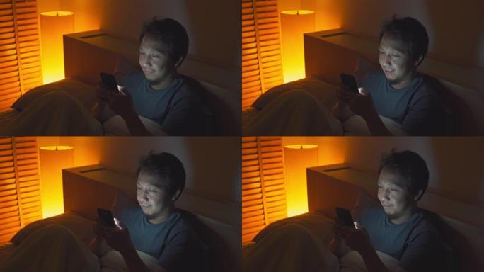 亚洲男子晚上在床上使用智能手机