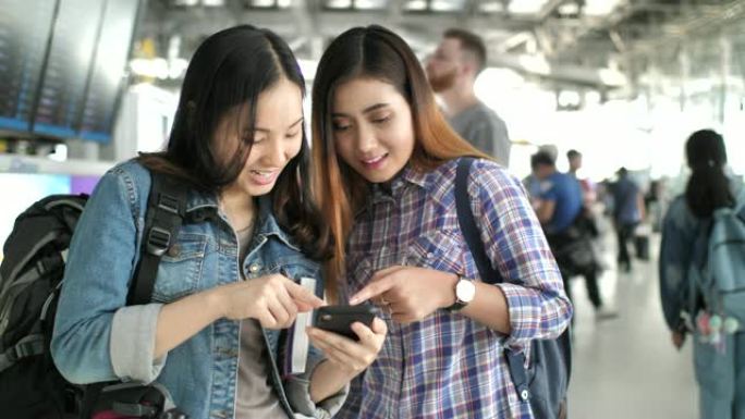 两名亚洲妇女在航站楼机场通过智能手机检查航班并在线办理登机手续