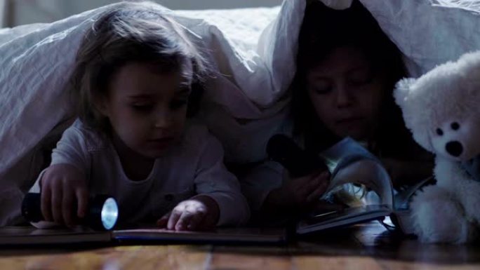 一个晚上在被窝下的小女孩读一本冒险和幻想的书，手里拿着火炬让自己发光。