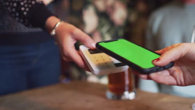 使用手机上的移动支付应用程序在酒吧中支付账单的客户特写-慢动作拍摄