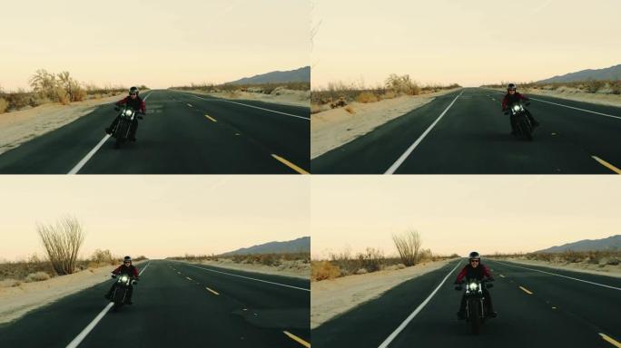 快乐的人骑着老式黑色摩托车在日落时沿着沙漠高速公路行驶