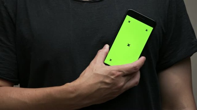 穿着黑色t恤的亚洲男子拿着绿色屏幕的智能手机，并指向屏幕。