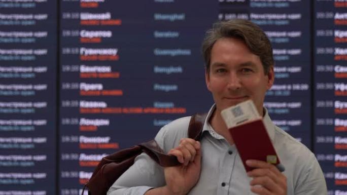 英俊的商人拿着行李护照和登机牌，在机场面对镜头微笑