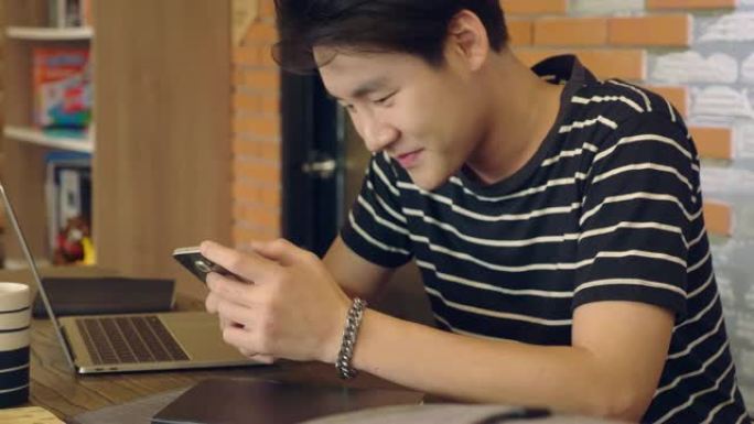 年轻的亚洲男子在咖啡馆餐桌上用智能手机发短信
