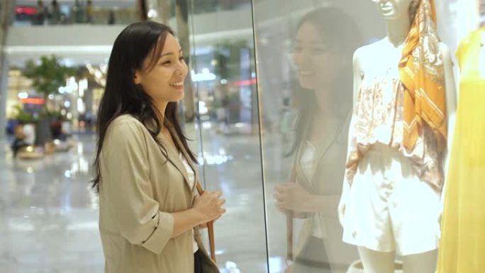 年轻的亚洲妇女在商店橱窗里看着手表和购物中心的奢侈品