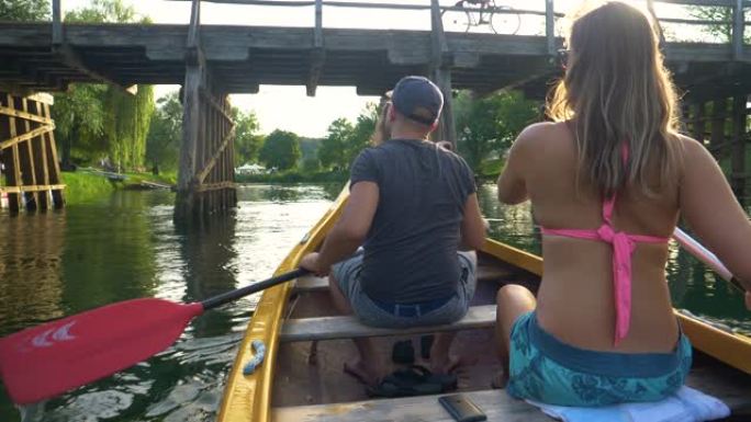 特写: 男人和女人沿着平静的河流和桥下划着独木舟