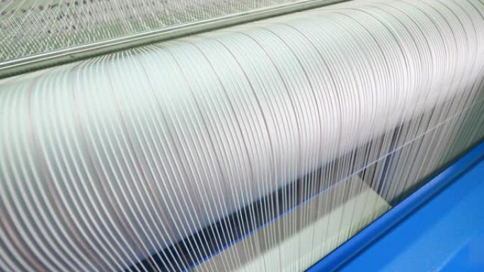 一台织机在一家纺织厂工作，卷着白线。