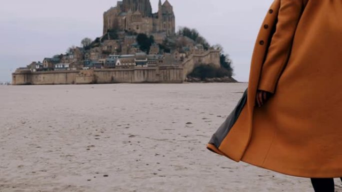 特写时尚快乐旅游女人在史诗圣米歇尔山城堡慢动作的柔软海沙上缓慢行走。