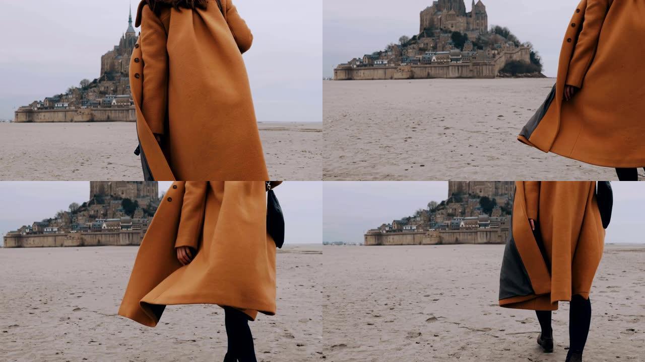 特写时尚快乐旅游女人在史诗圣米歇尔山城堡慢动作的柔软海沙上缓慢行走。