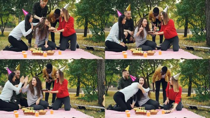 年轻人在生日那天祝贺女孩带着蛋糕拥抱和亲吻她，女人在公园的户外聚会上吹蜡烛，欢笑和欢欣鼓舞。