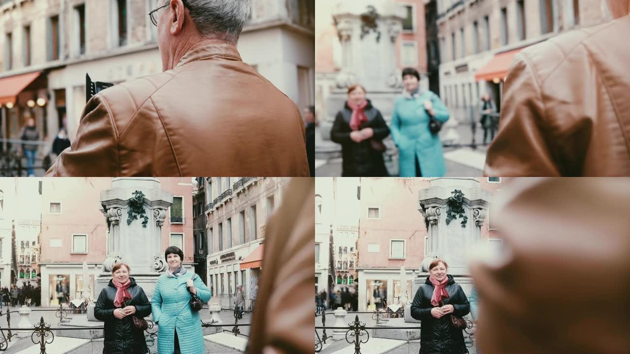 快乐的欧洲高级男子在度假期间拍摄了两名老年妇女在意大利威尼斯街上摆姿势的智能手机照片。