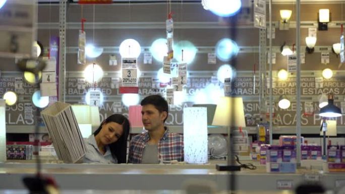 拉丁美洲的年轻夫妇在一家五金店里看着灯，为他们的新家微笑
