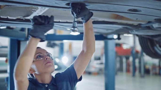 一名在汽车服务公司工作的女机械师的肖像镜头。授权女性戴手套和使用棘轮下的汽车。现代洁净车间。