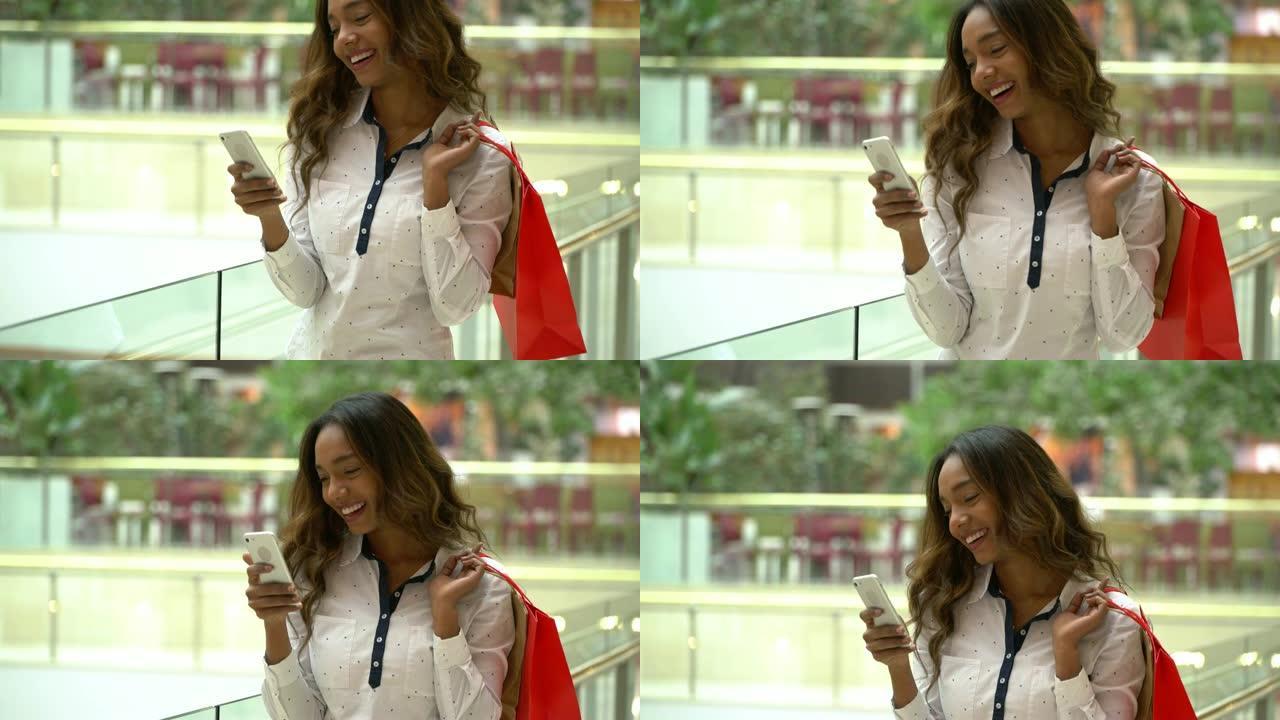 购物中心的非裔美国美女拿着购物袋在智能手机上发短信