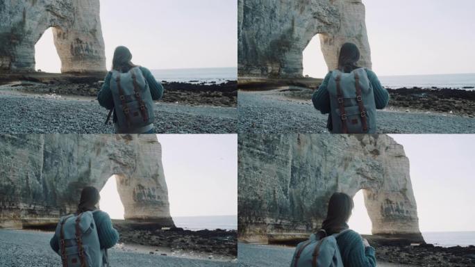 后视快乐的旅游女人，背着背包，沿着美丽的海岸探索白色拱形岩石，靠近埃特雷塔慢动作