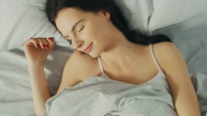 美丽的年轻黑发女人的肖像在清晨迷人地睡在她的床上。安静睡觉的女孩甜美温暖的景色。自上而下的旋转相机拍