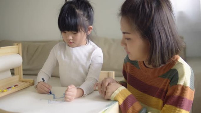 快乐的亚洲男孩和他的母亲在家里的客厅用蜡笔画画。