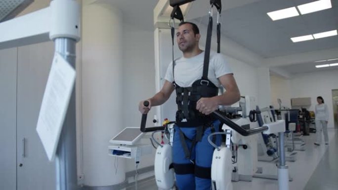在康复中心的外骨骼机器人上的英俊男性患者学习再次走路，看上去很专注