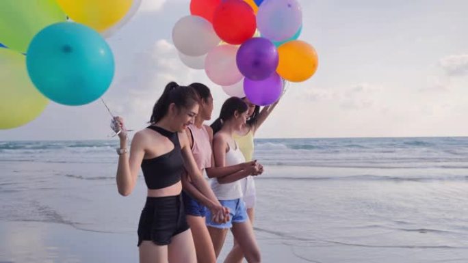 一群女朋友带着气球在蓝天的背景下在海滩上奔跑。幸福的朋友在夏日阳光明媚的阳光下在海滩上玩耍。假期-i