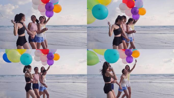 一群女朋友带着气球在蓝天的背景下在海滩上奔跑。幸福的朋友在夏日阳光明媚的阳光下在海滩上玩耍。假期-i