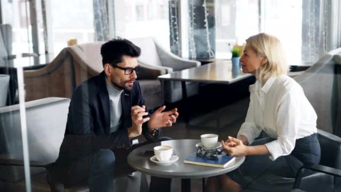 中年大胡子男子在咖啡馆与女性商业伙伴讨论交易