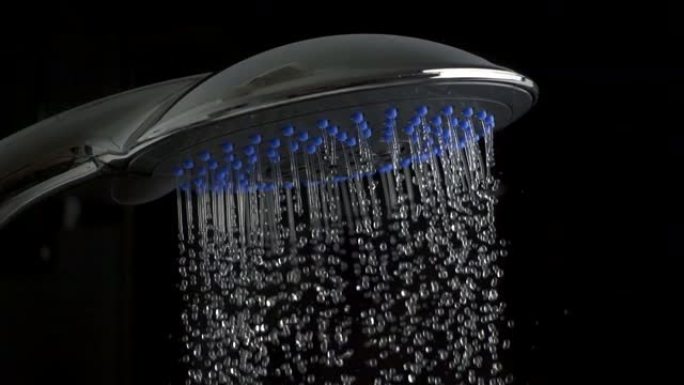 淋浴喷头特写。许多水滴来自银色玻璃淋浴喷头，黑色背景上有蓝色嵌入。舒适的概念。慢动作镜头