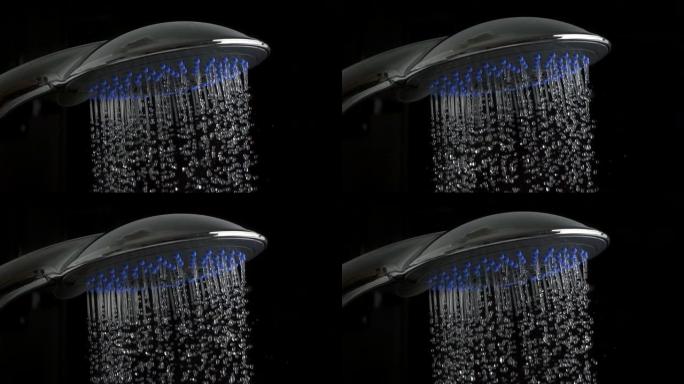 淋浴喷头特写。许多水滴来自银色玻璃淋浴喷头，黑色背景上有蓝色嵌入。舒适的概念。慢动作镜头