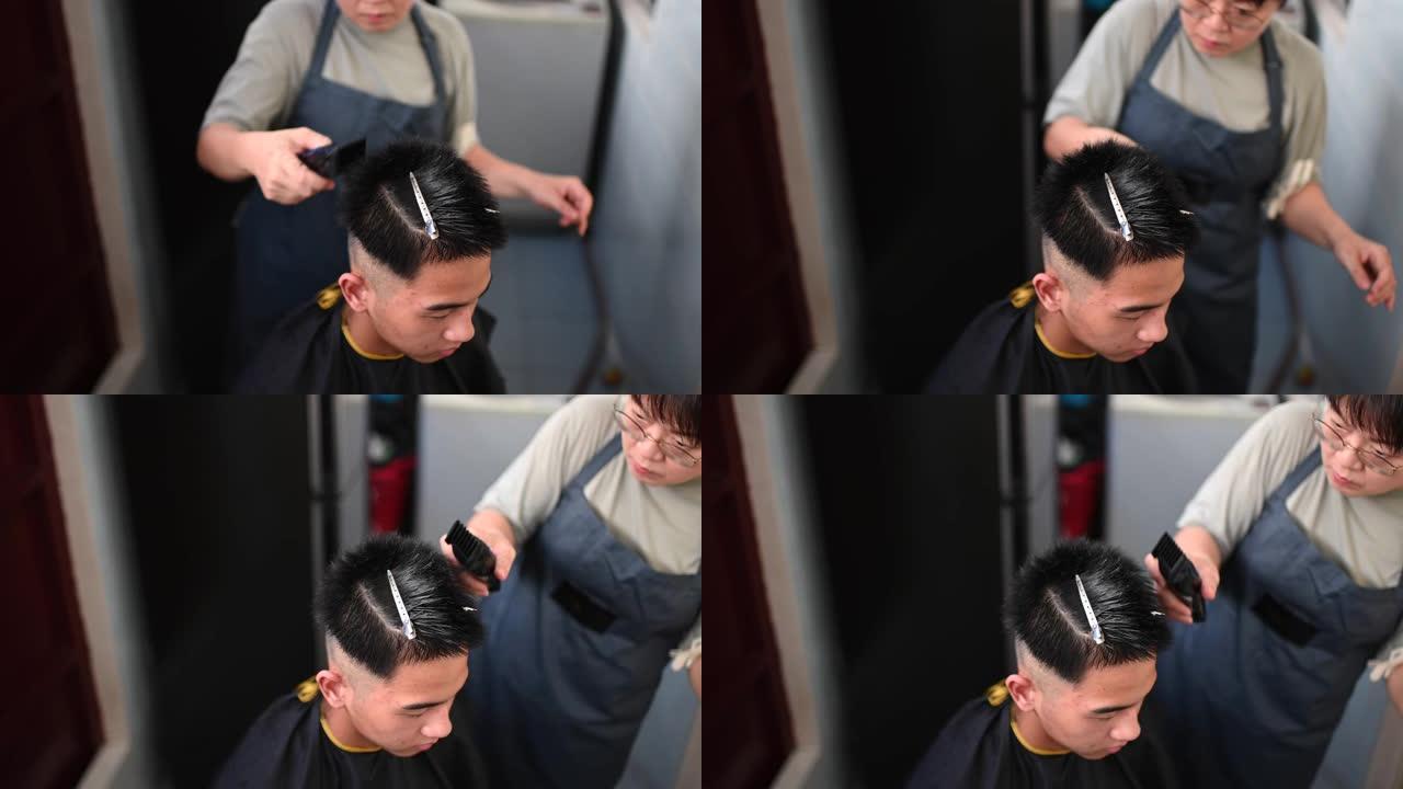 由于旅行禁令，一名亚洲华裔中年妇女正在厨房为儿子剪头发和修剪头发