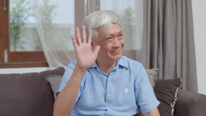 肖像亚洲中国高级男子在家里微笑快乐。年长的男性放松露齿的微笑，看着相机，而躺在沙发在家里的客厅里的概