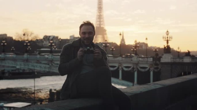开朗浪漫的旅游男人拍照，在梦幻的巴黎慢动作中微笑着在秋天的塞纳河日落河岸上。