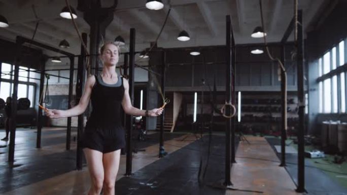 美丽的年轻高个子金发女子在大型健身房慢动作中用跳绳锻炼。积极健康的生活方式。