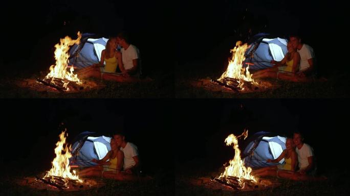 特写: 饥饿的夫妇在篝火旁拥抱，晚上烤香肠。