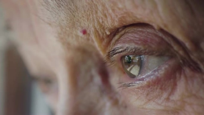 一位老年妇女的绿色眼睛向窗外望去的微距镜头。