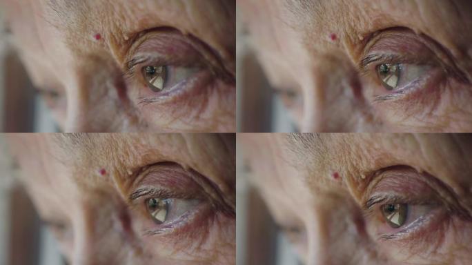 一位老年妇女的绿色眼睛向窗外望去的微距镜头。