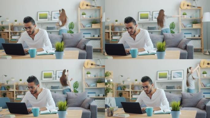阿拉伯商人在家里用笔记本电脑工作，而妻子在背景中跳舞