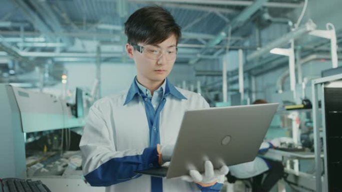 在高科技工厂，亚洲工程师使用笔记本电脑进行编程，为印刷电路板表面安装装配线拾取和放置电子机械。用SM