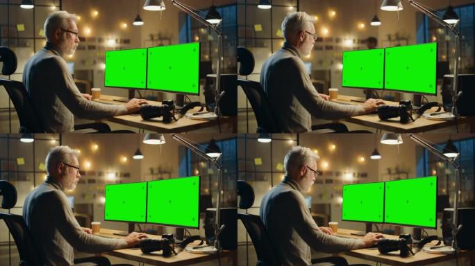 坐在办公桌前的创意中年设计师使用带有两个绿色模拟屏幕的台式计算机。专业办公室员工晚上在工作室工作